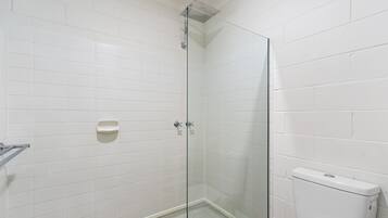 Et badeværelse med hvide flisevægge, et brusekabine i glas og et hvidt toilet.