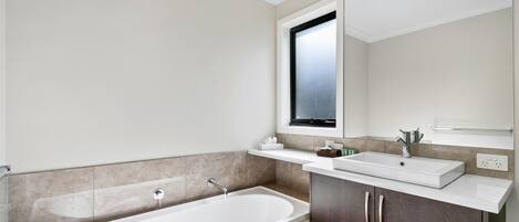A modern bathroom with a freestanding bathtub, a vanity with a mirror, and a window above the sink.