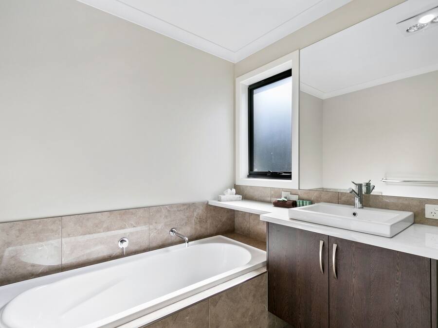 Un baño moderno con una bañera independiente, un tocador con espejo y una ventana sobre el lavamanos.