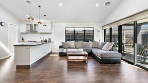 A modern living space with a kitchen, a seating area with a sofa and ottoman, and large windows offering a view. - The Aspen & Apartments (Sale)
