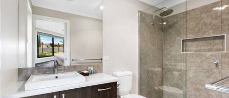 A modern bathroom with a large mirror, a sink, a toilet, and a glass-enclosed shower.