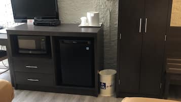 Una habitación de hotel con un mueble de madera oscura, un televisor, un microondas y un pequeño cubo de basura.