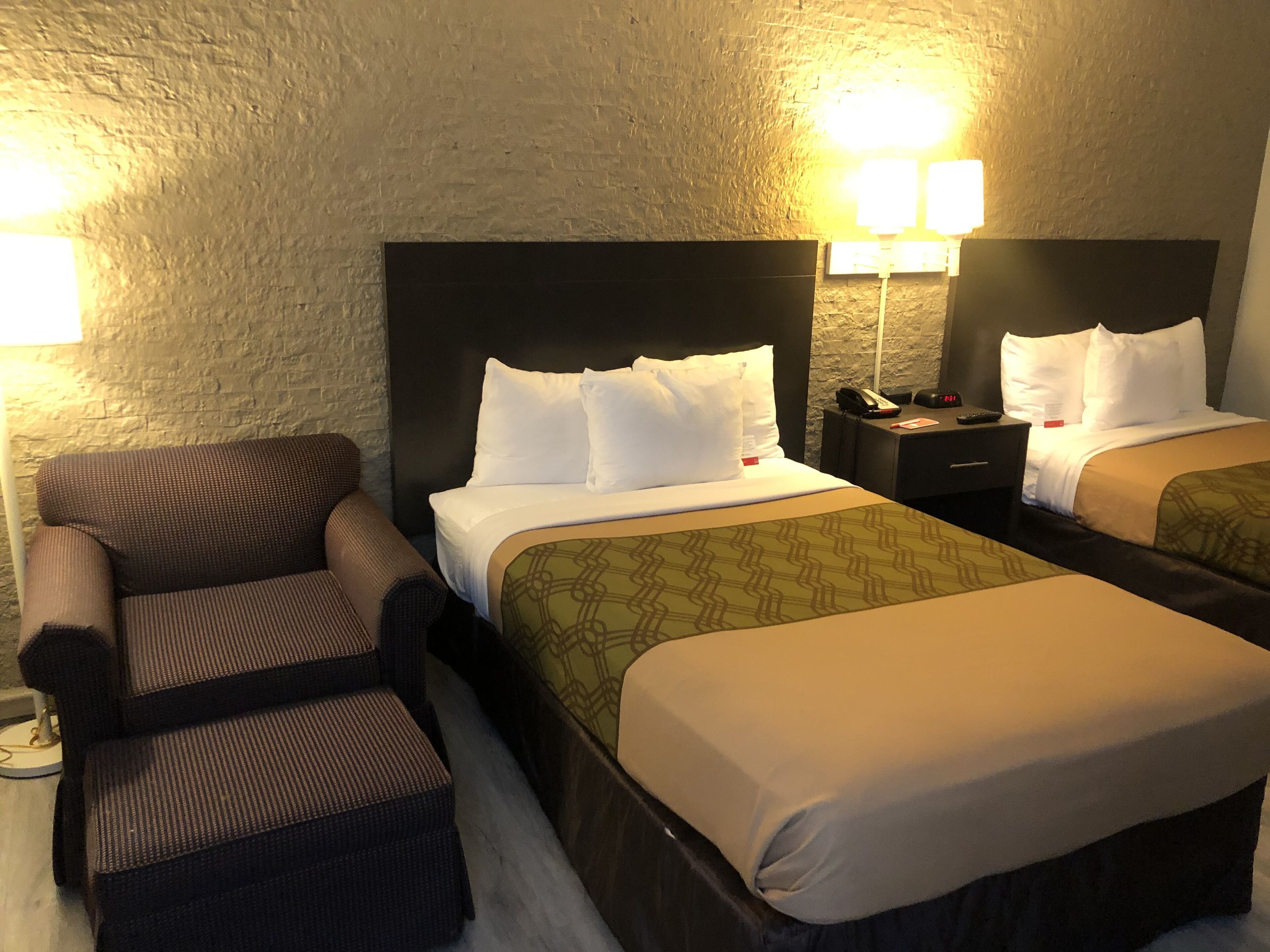 A hotel room with two beds, a sofa, and a nightstand with a lamp.