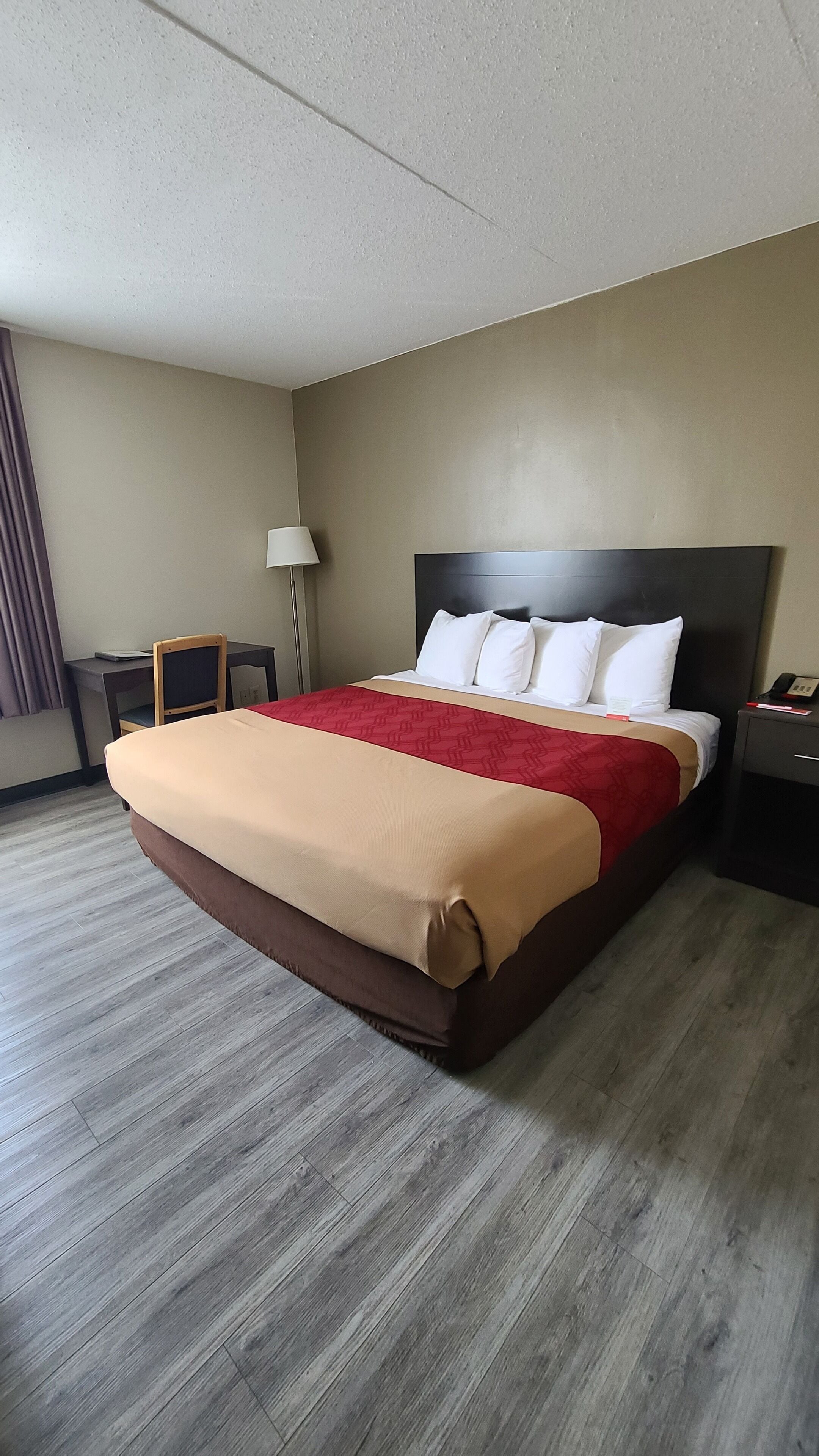 A hotel room with a large bed, a desk, a chair, a lamp, and a telephone on the nightstand.