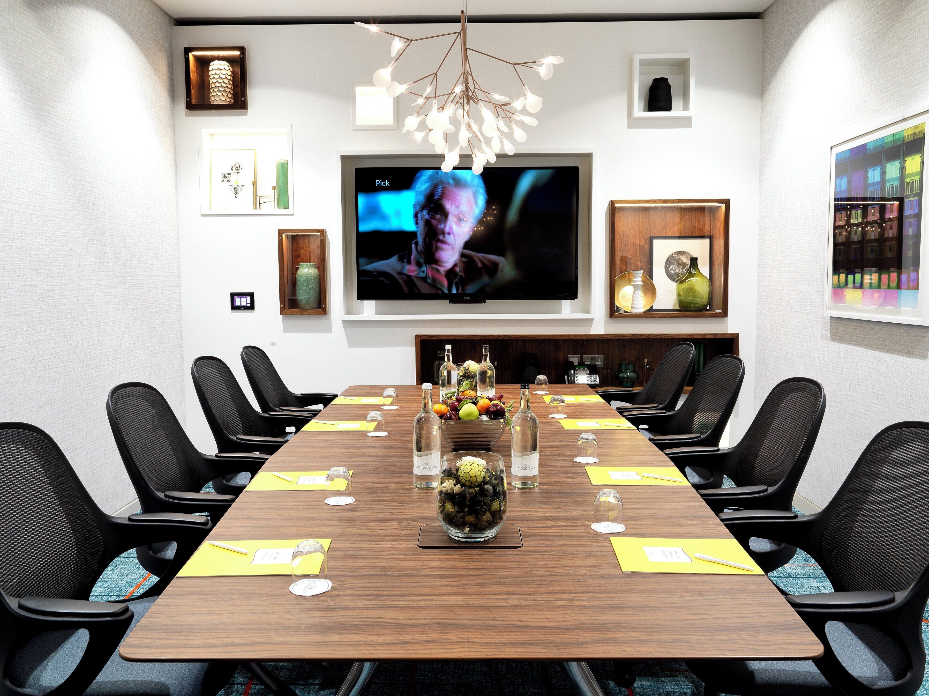 A conference room with a long table, black chairs, a TV screen, and various decorative items.