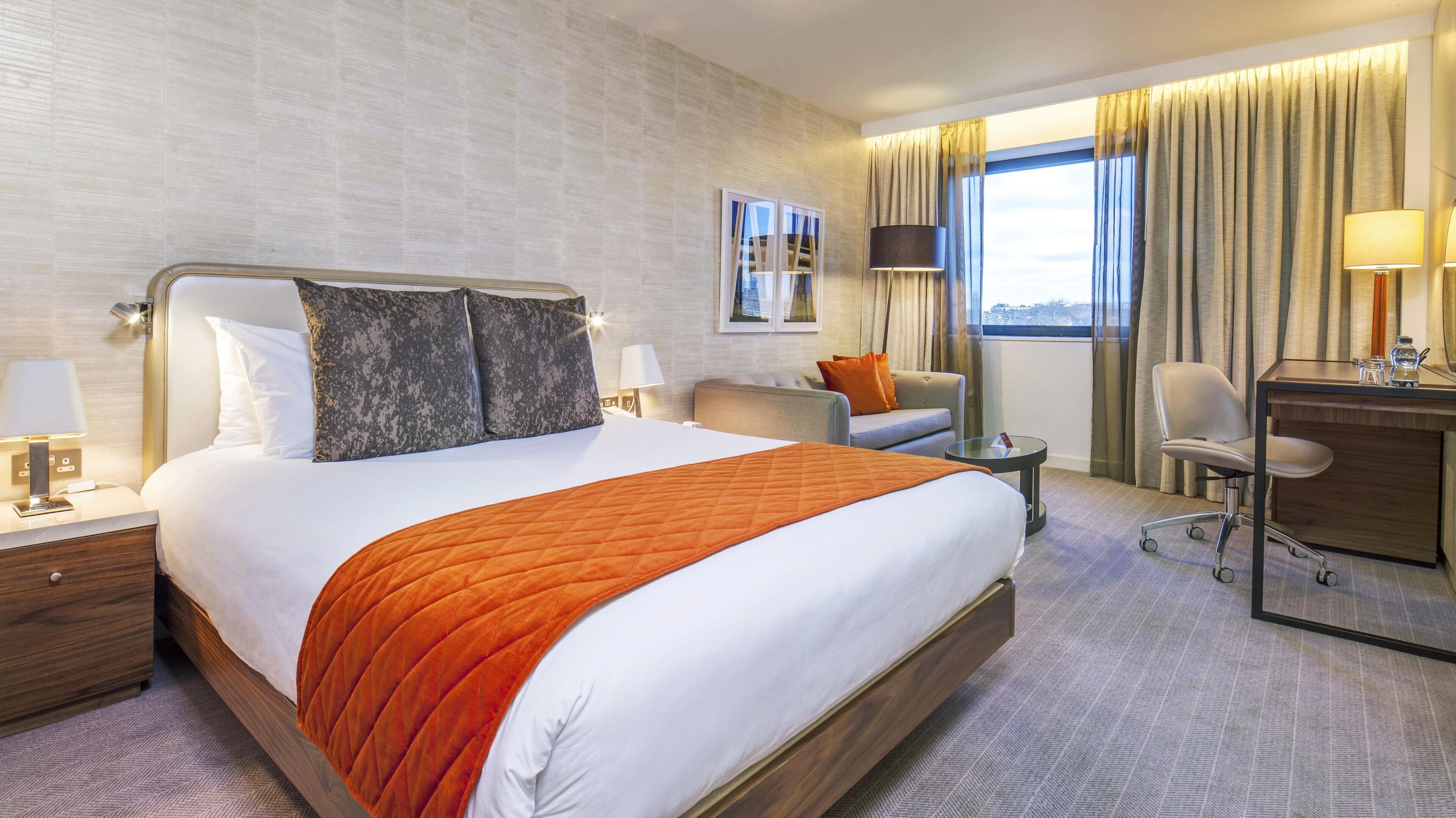 Ein Hotelzimmer mit einem großen Bett, einem Schreibtisch, einem Sessel, einer Couch und Blick auf die Stadt.