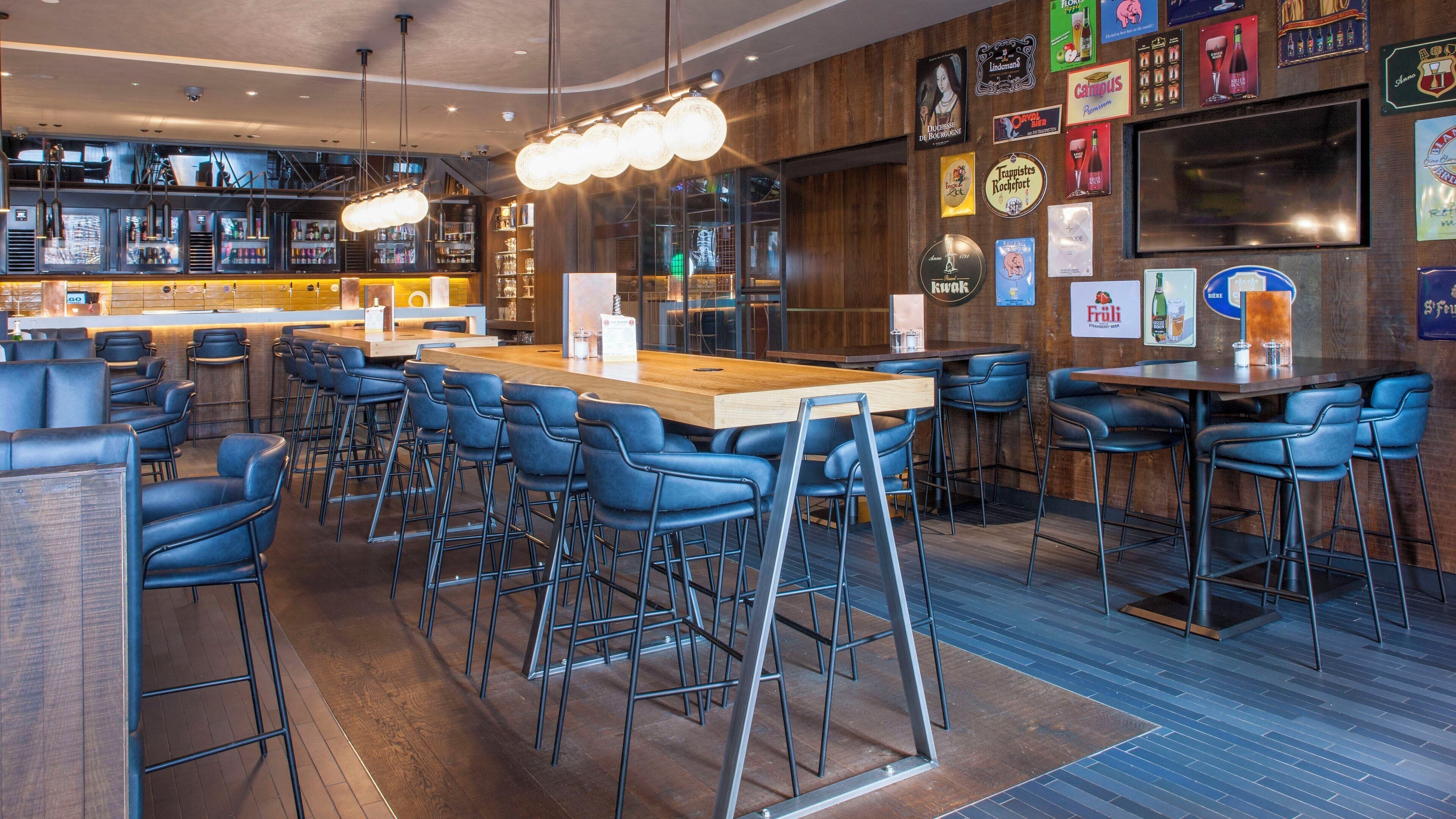 Un espace bar avec des tabourets hauts, un long comptoir en bois et diverses bouteilles de bière et de spiritueux exposées sur des étagères.