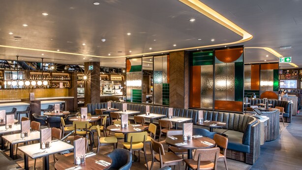 Un restaurante moderno con cabinas y mesas, una zona de bar y un letrero de salida verde.