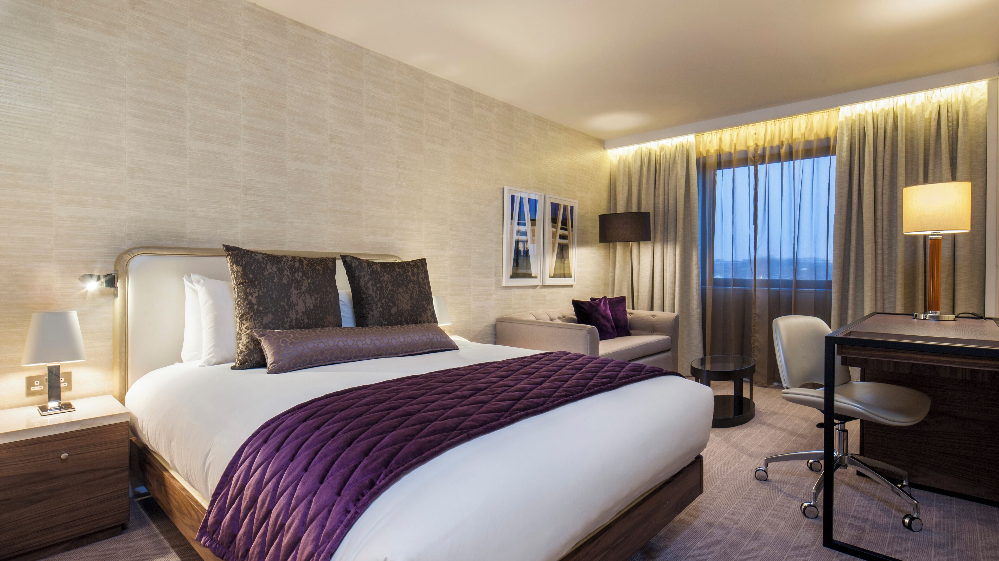 A hotel room with a large bed, a desk, a chair, and a view of the city.