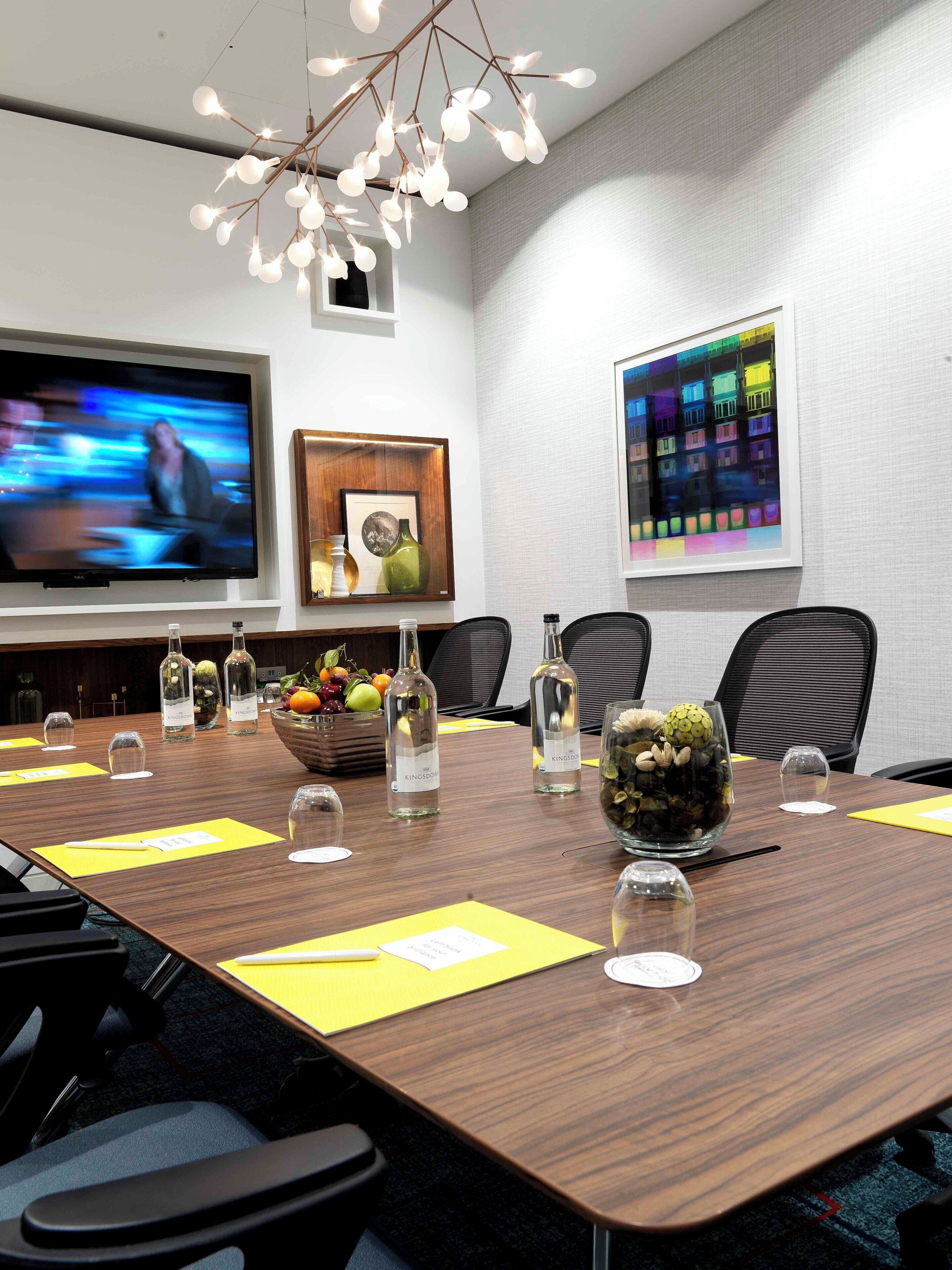 A conference room with a long table, chairs, a television, framed artwork, and a decorative centerpiece.