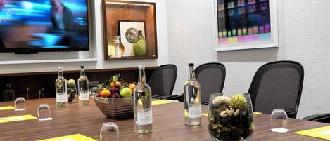 A conference room with a long table, chairs, a television, framed artwork, and a decorative centerpiece.