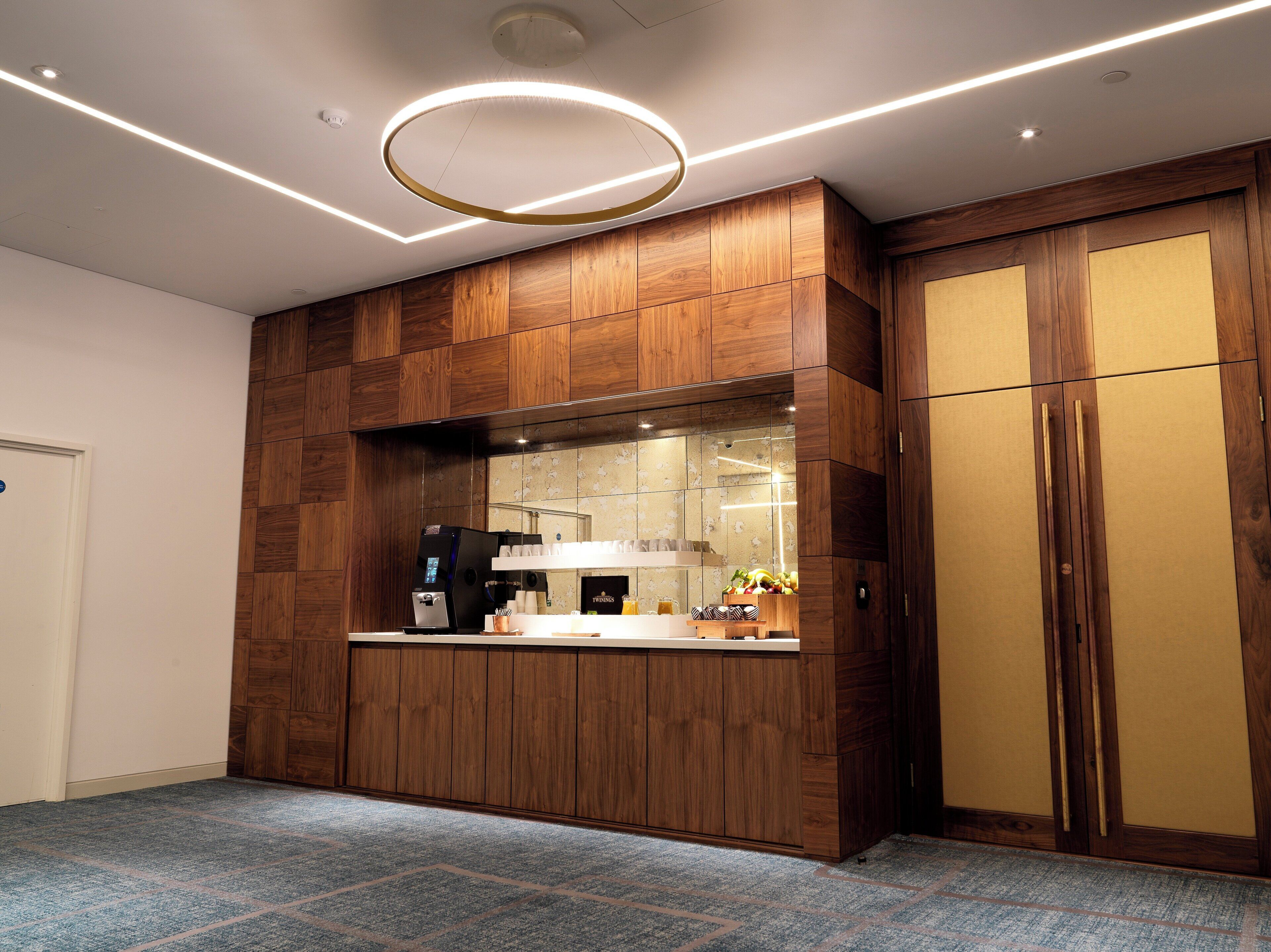 A modern kitchen with wooden cabinetry, a built-in coffee machine, and a fruit display.