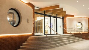 A hotel entrance with a glass door, a staircase, and a circular mirror on the wall. - Crowne Plaza London - Kings Cross by IHG (London)