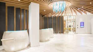 Una moderna zona de recepción con techo curvo, un panel informativo digital y un área de descanso con sillones.