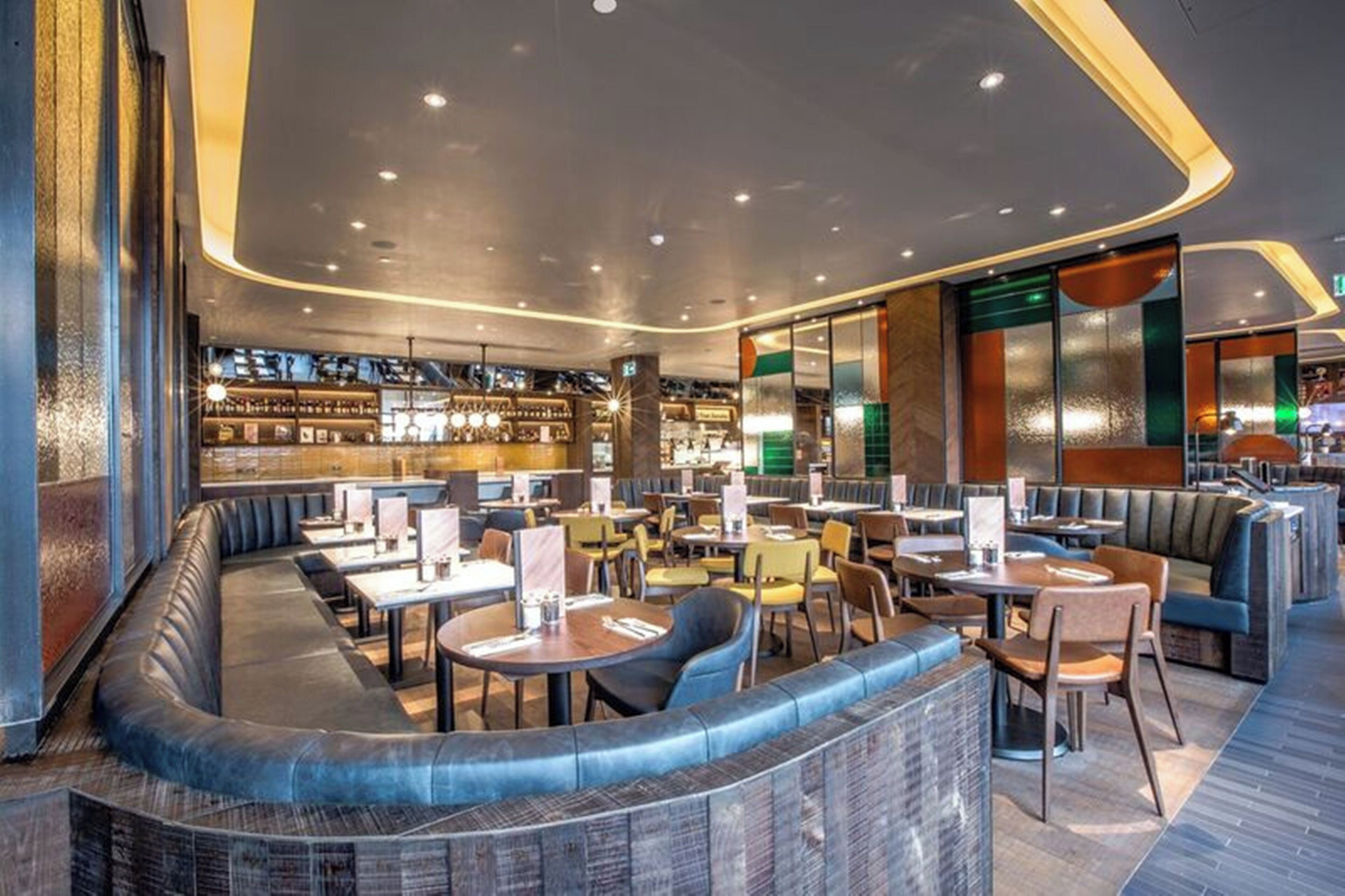 Un restaurant moderne doté d’un espace salon aux lignes courbes, d’un bar et d’un mélange de tables et de banquettes.