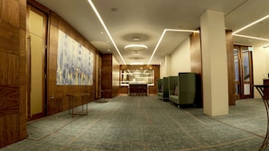 Un vestíbulo de hotel con paneles de madera, un cuadro abstracto de gran tamaño, un mostrador de recepción y asientos verdes.