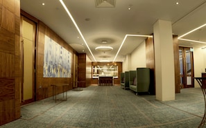 Un vestíbulo de hotel con paneles de madera, un cuadro abstracto de gran tamaño, un mostrador de recepción y asientos verdes.