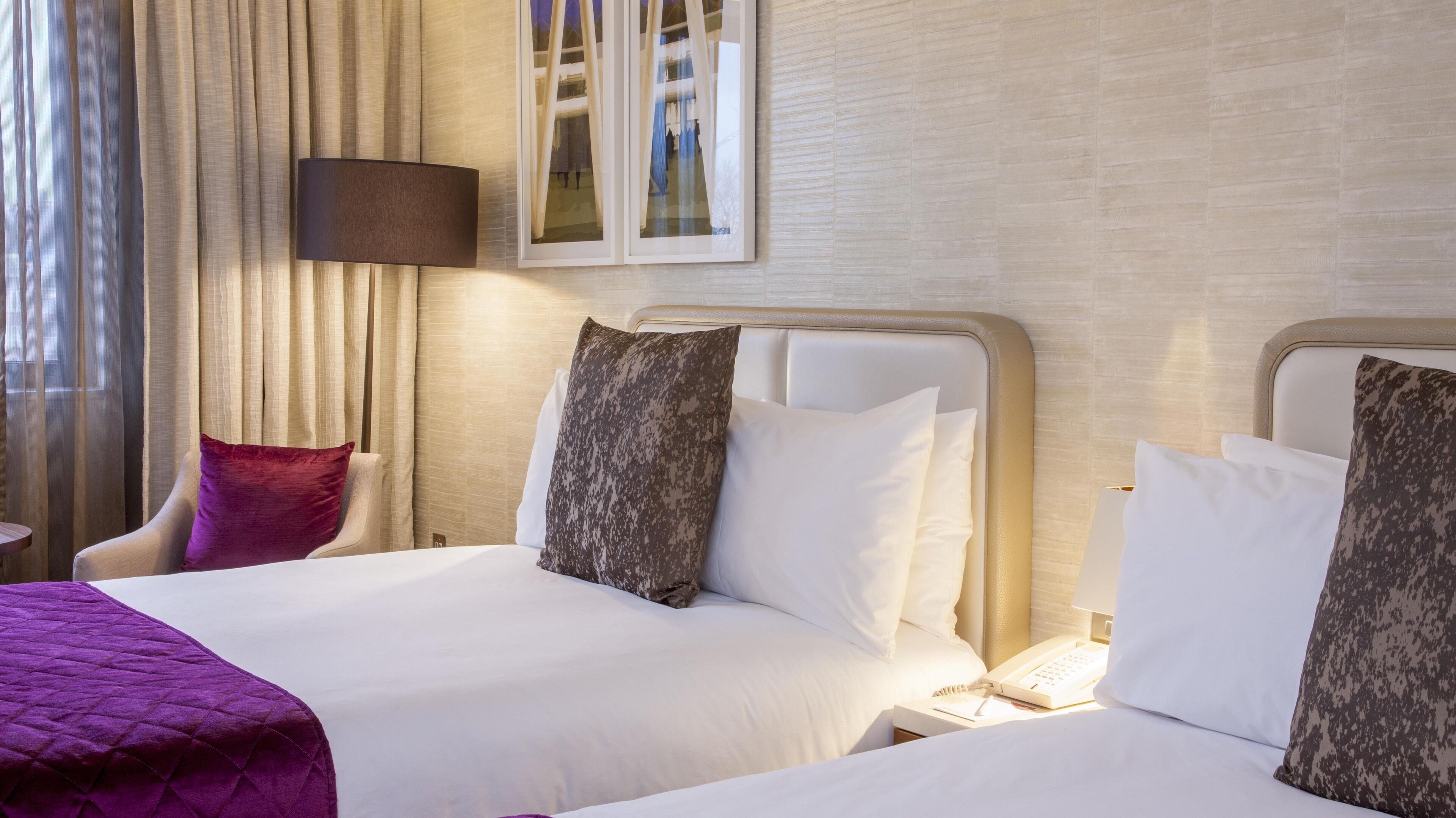 A hotel room with two beds, a chair, a desk with a phone, and a window with curtains.