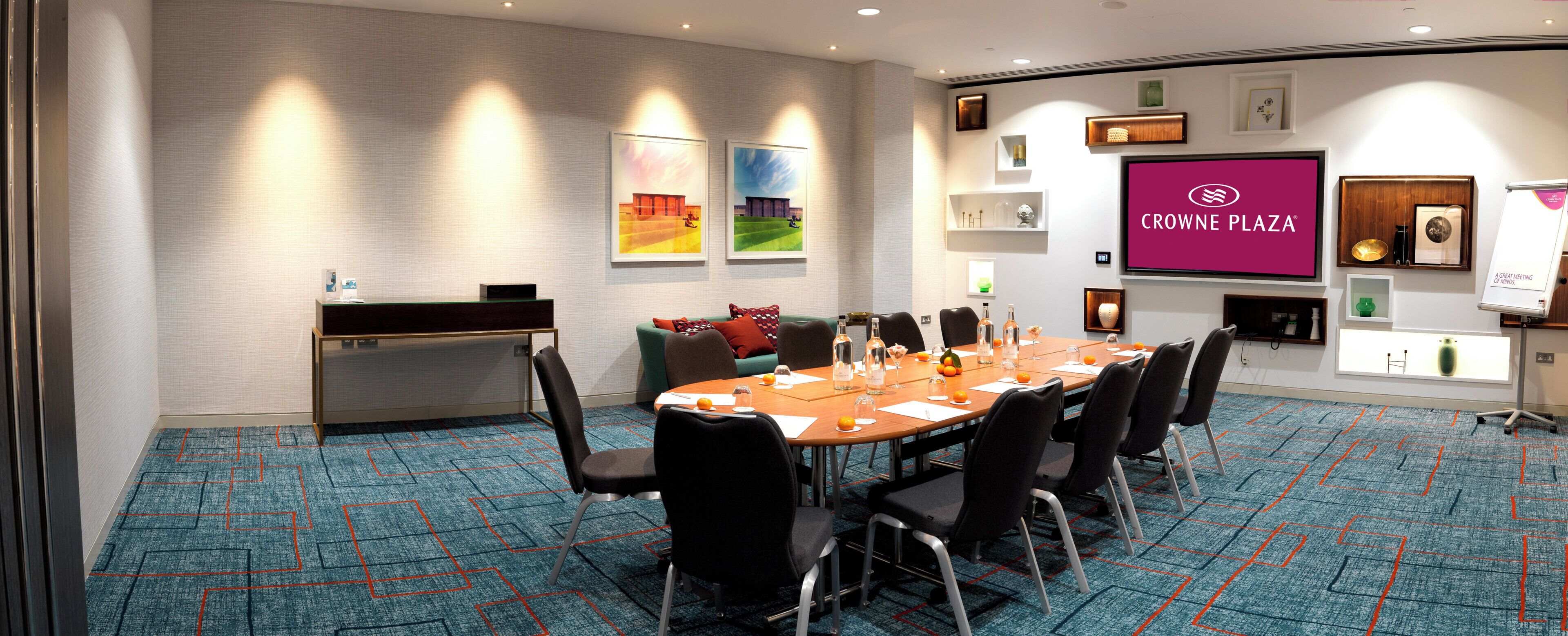 Een vergaderruimte met een lange tafel, stoelen, een receptiebalie en kunstwerken aan de muren.