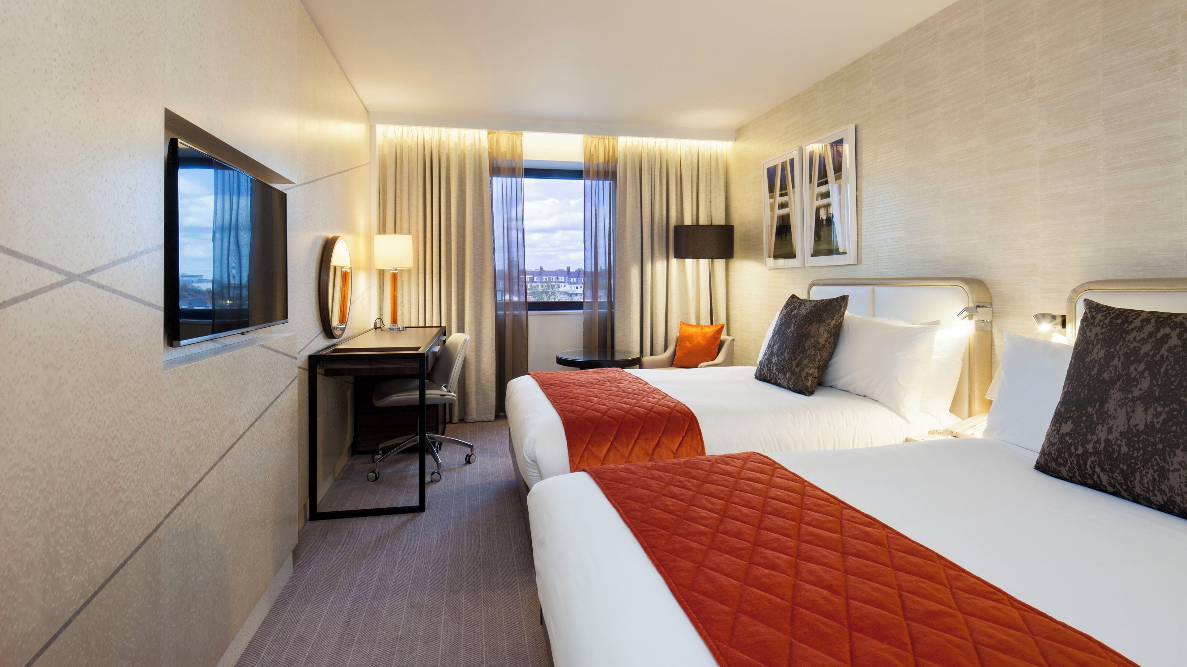 A hotel room with two beds, a desk, a chair, a small table, and a window with curtains.