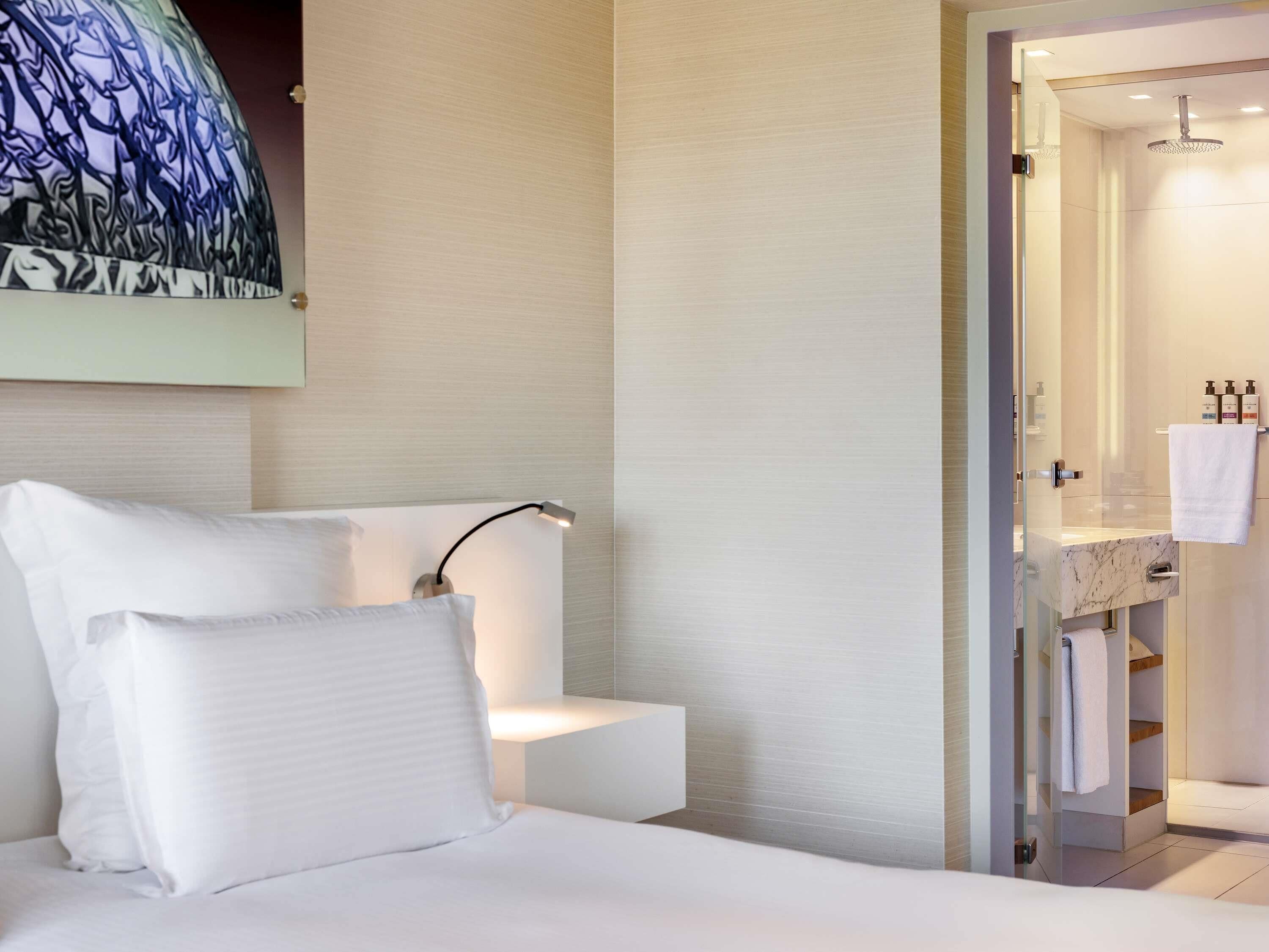 A hotel room with a bed, a bedside lamp, a shower area, and a wall-mounted artwork.
