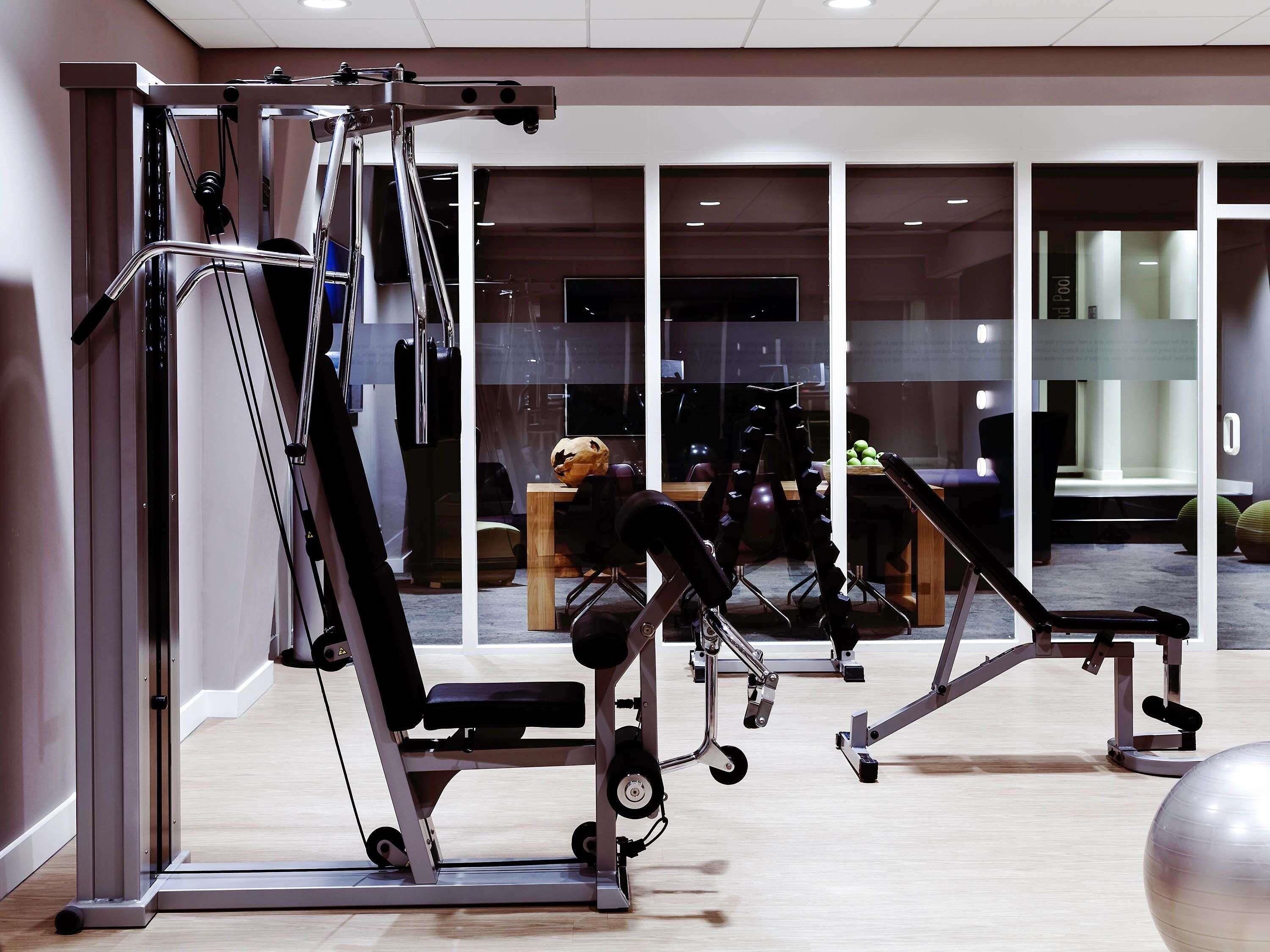 A gym with exercise equipment, a wooden table with apples, and a large window.