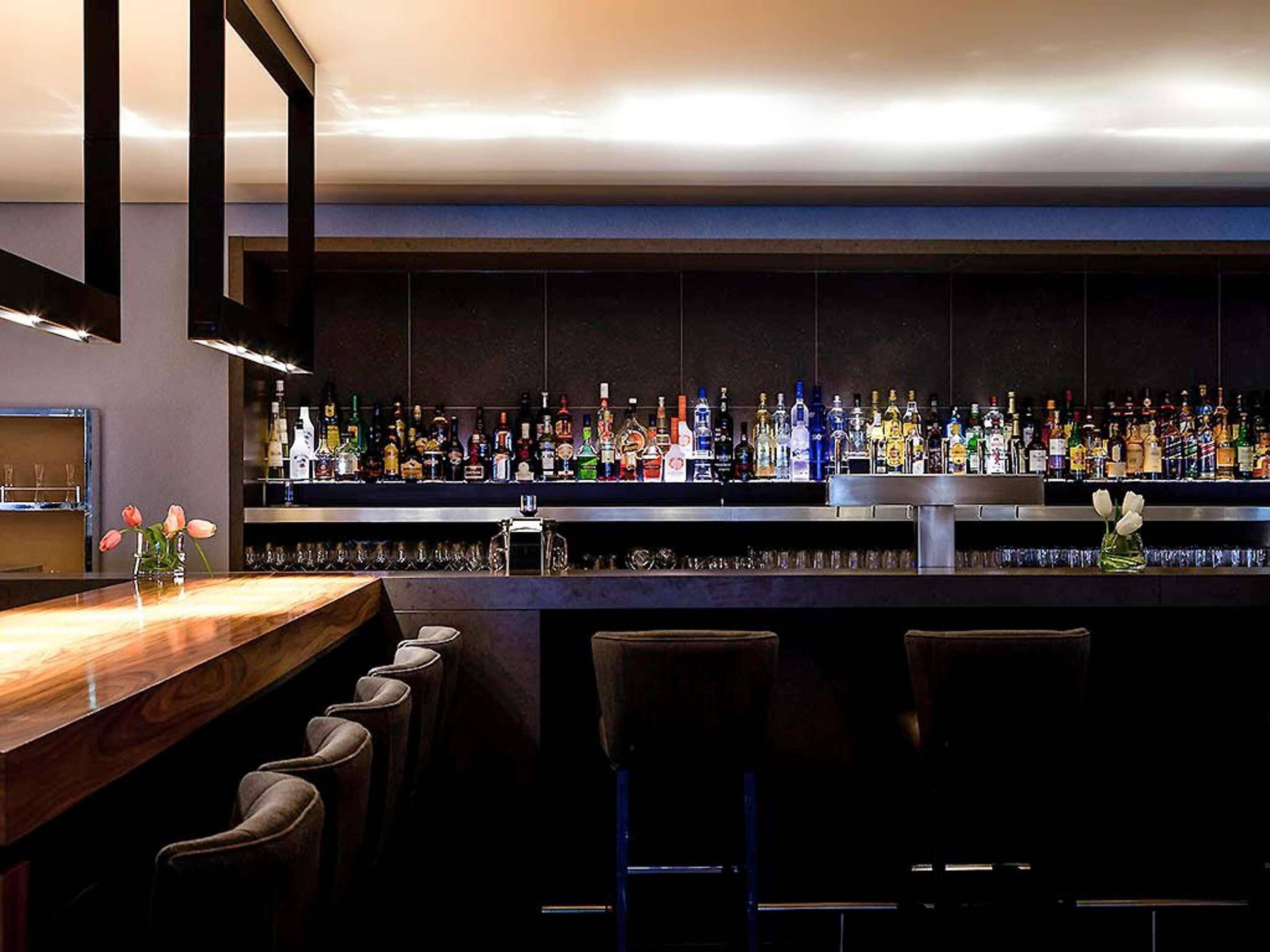 A bar area with a long counter, multiple stools, and a variety of bottles and glasses.