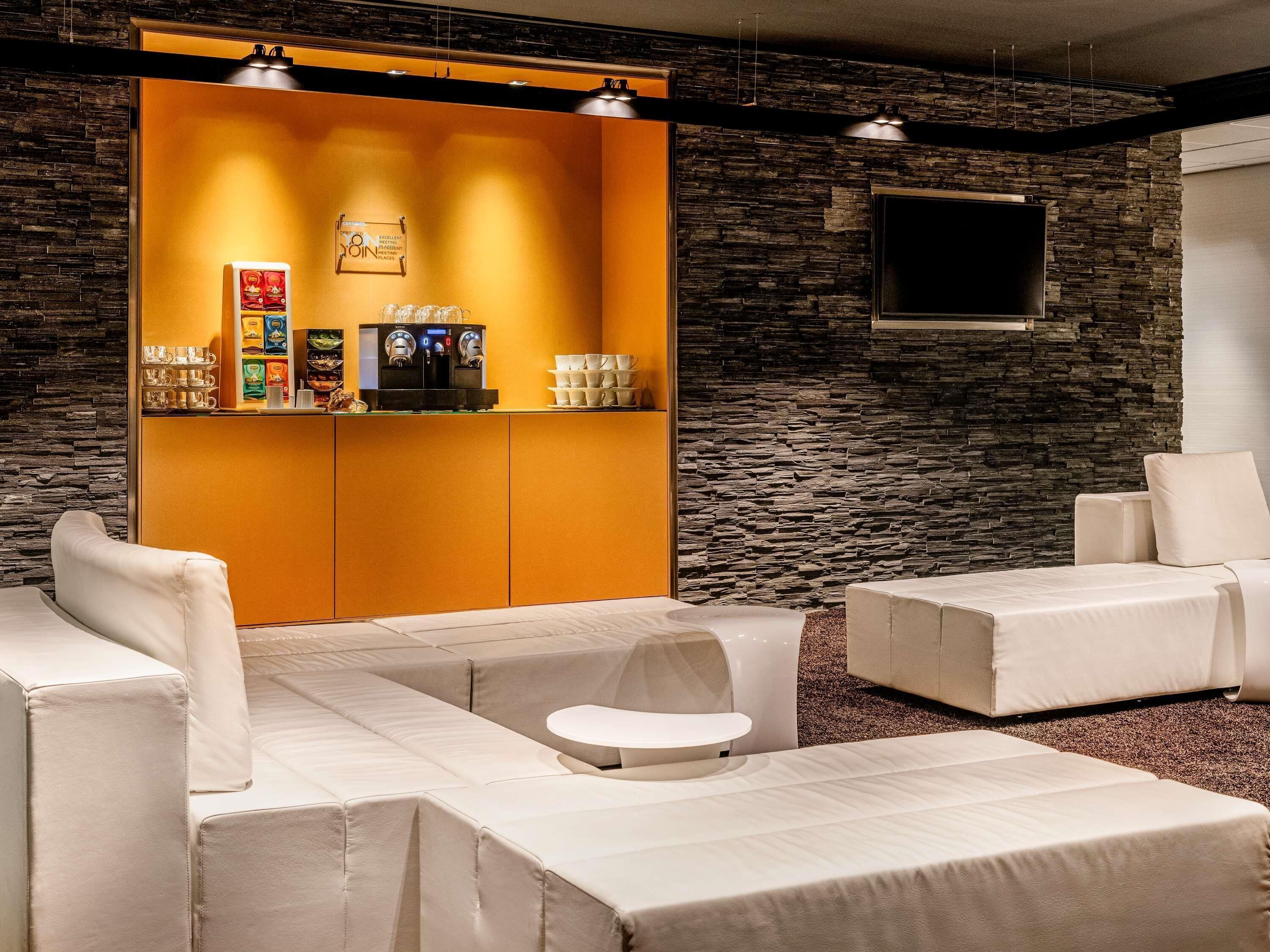 A modern lounge area with a coffee station, seating, and a stone wall.