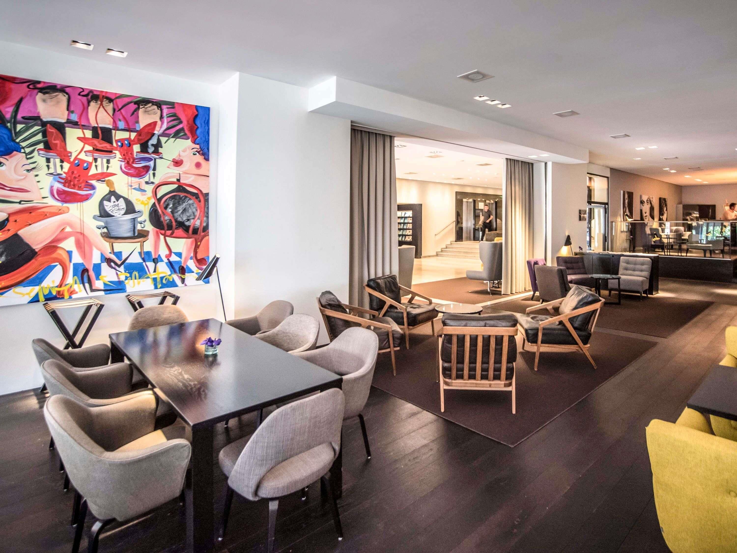 A modern hotel lobby with a dining area, a staircase, and a bar.
