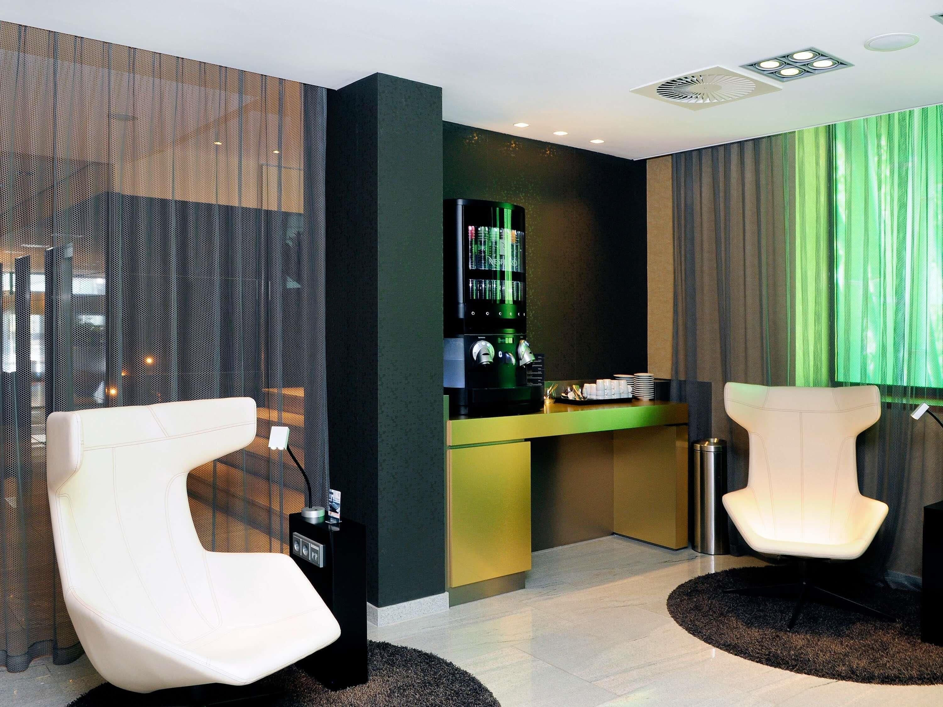 Eine moderne Hotelhalle mit einer Rezeption, zwei weißen Stühlen, einer grünen Theke und einem großen Fenster mit grünen Vorhängen.