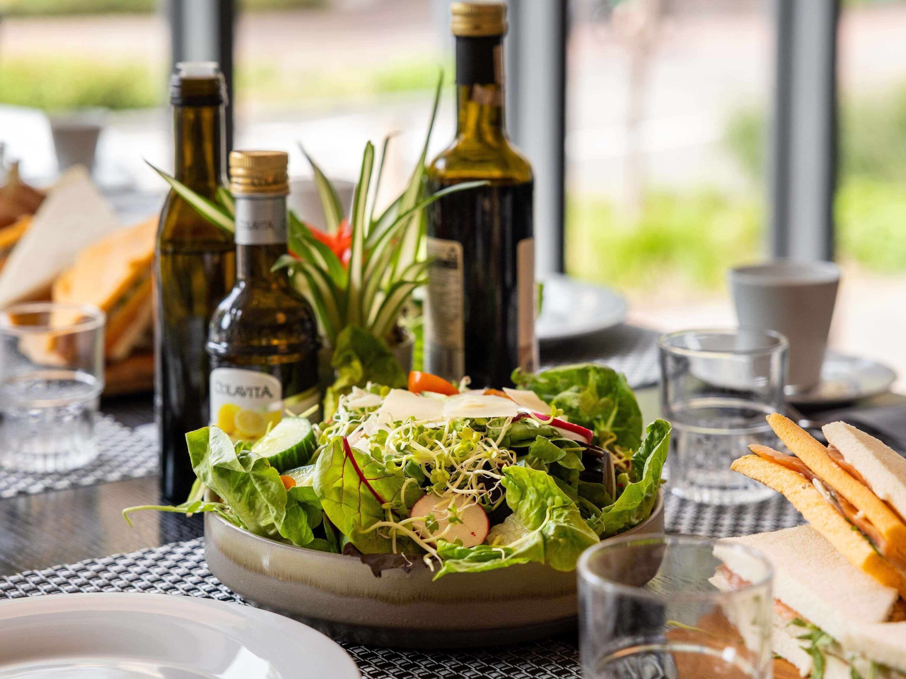 Een tafel met een saladekom, flesjes olijfolie en sandwiches.