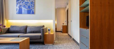 A modern hotel room with a grey sofa, a coffee table, a wooden TV stand, and a carpeted floor.