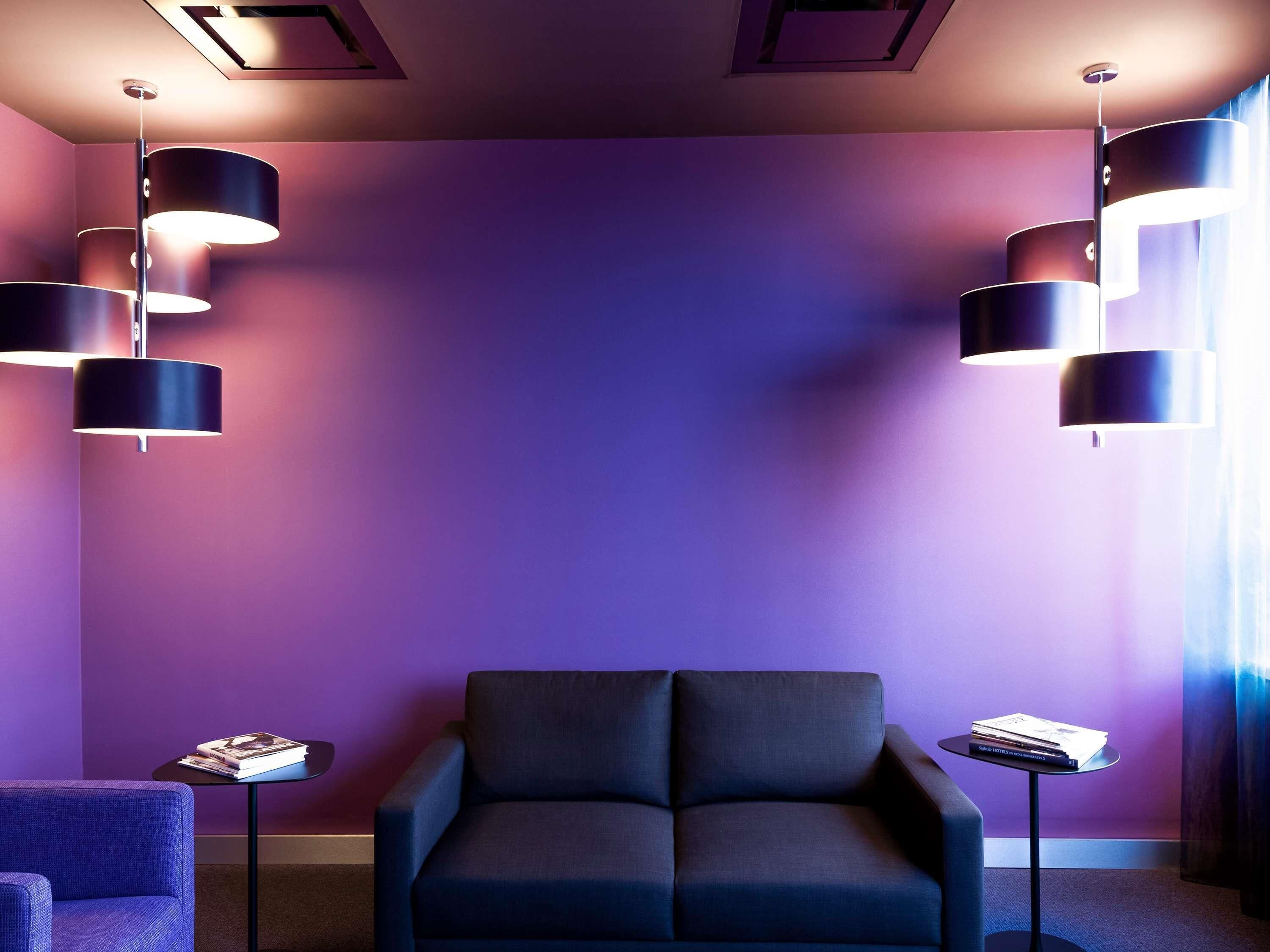 A modern room with a dark blue sofa, two small tables with magazines, and three pendant lights against a purple wall.