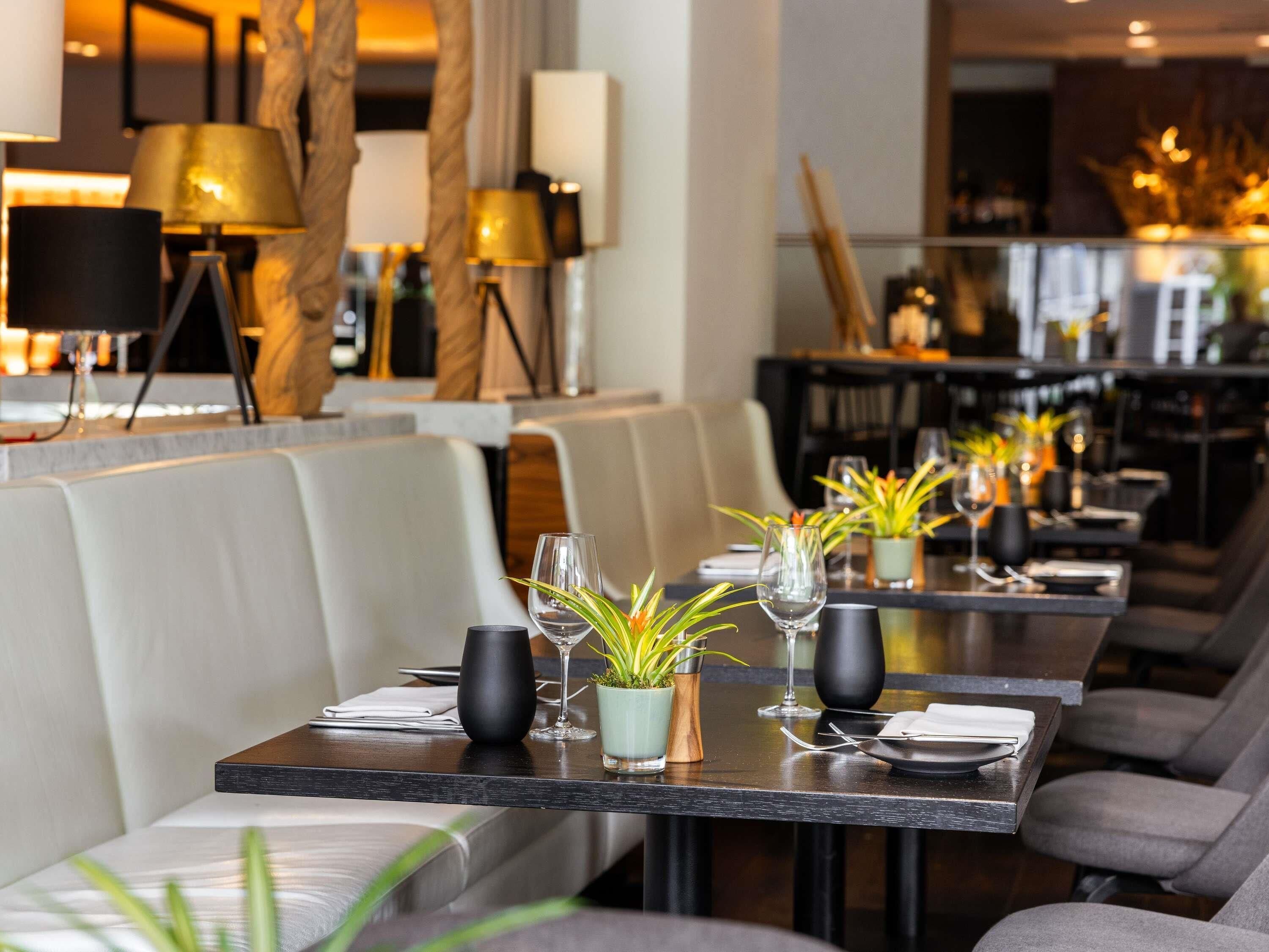 Un restaurant avec de longues tables, des sièges rembourrés et des plantes en pot.