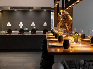 A restaurant with a long dining table set for a meal, a decorative wooden sculpture, and a counter with kitchen equipment. - Pullman Eindhoven Cocagne (Eindhoven)