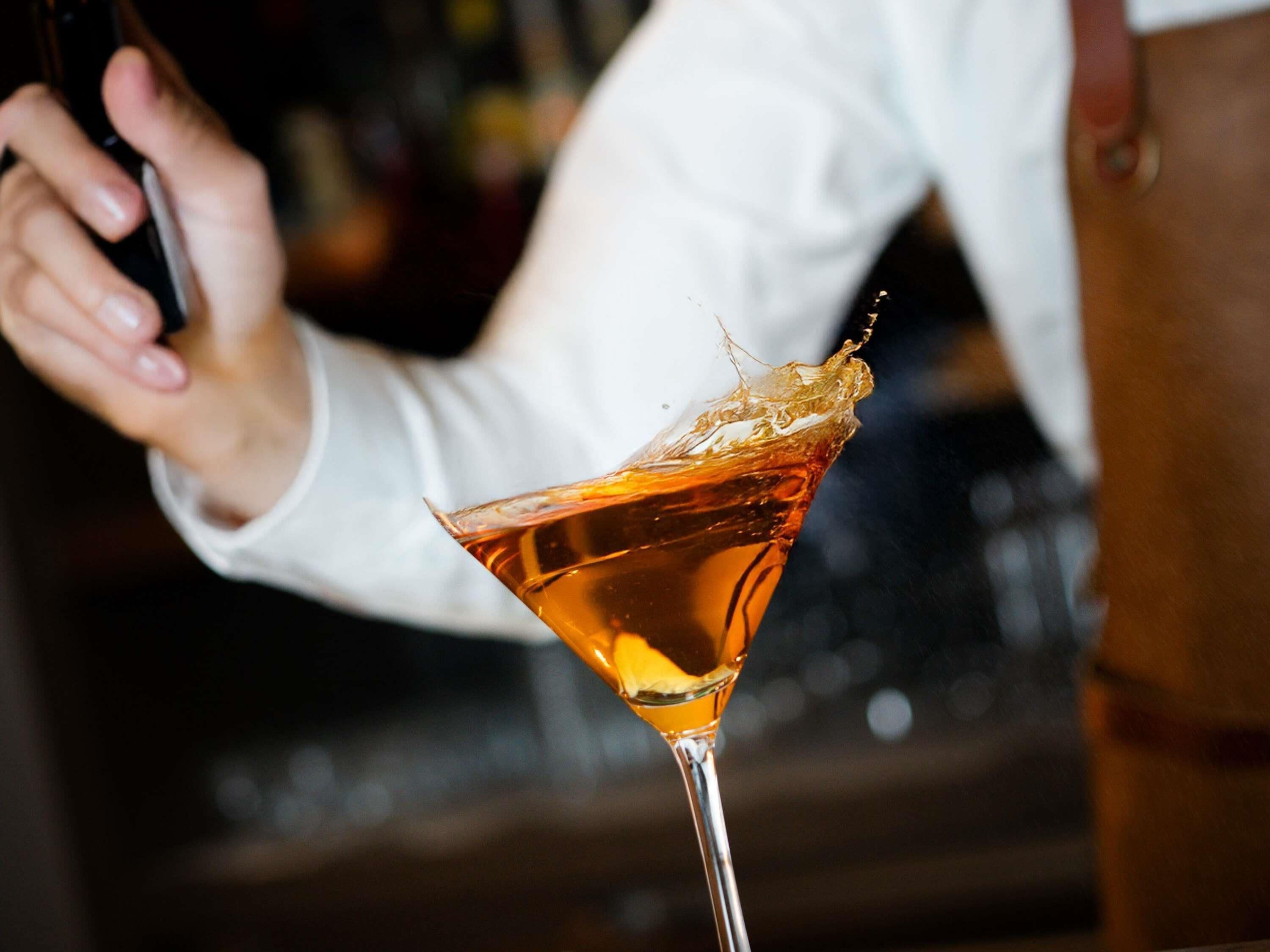 A person pouring a drink into a martini glass.