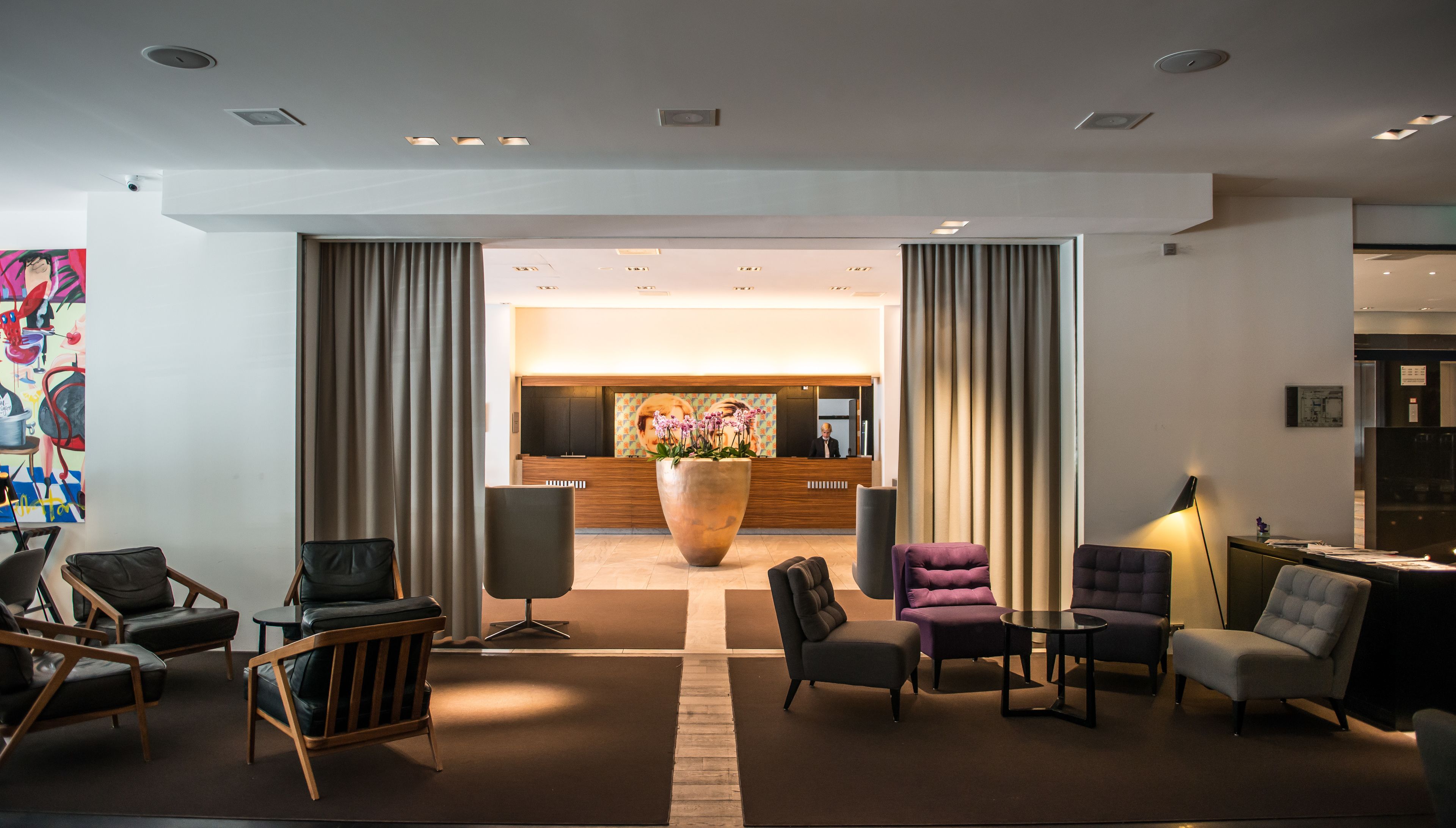 A modern lobby with a reception desk, a large potted plant, and seating areas.