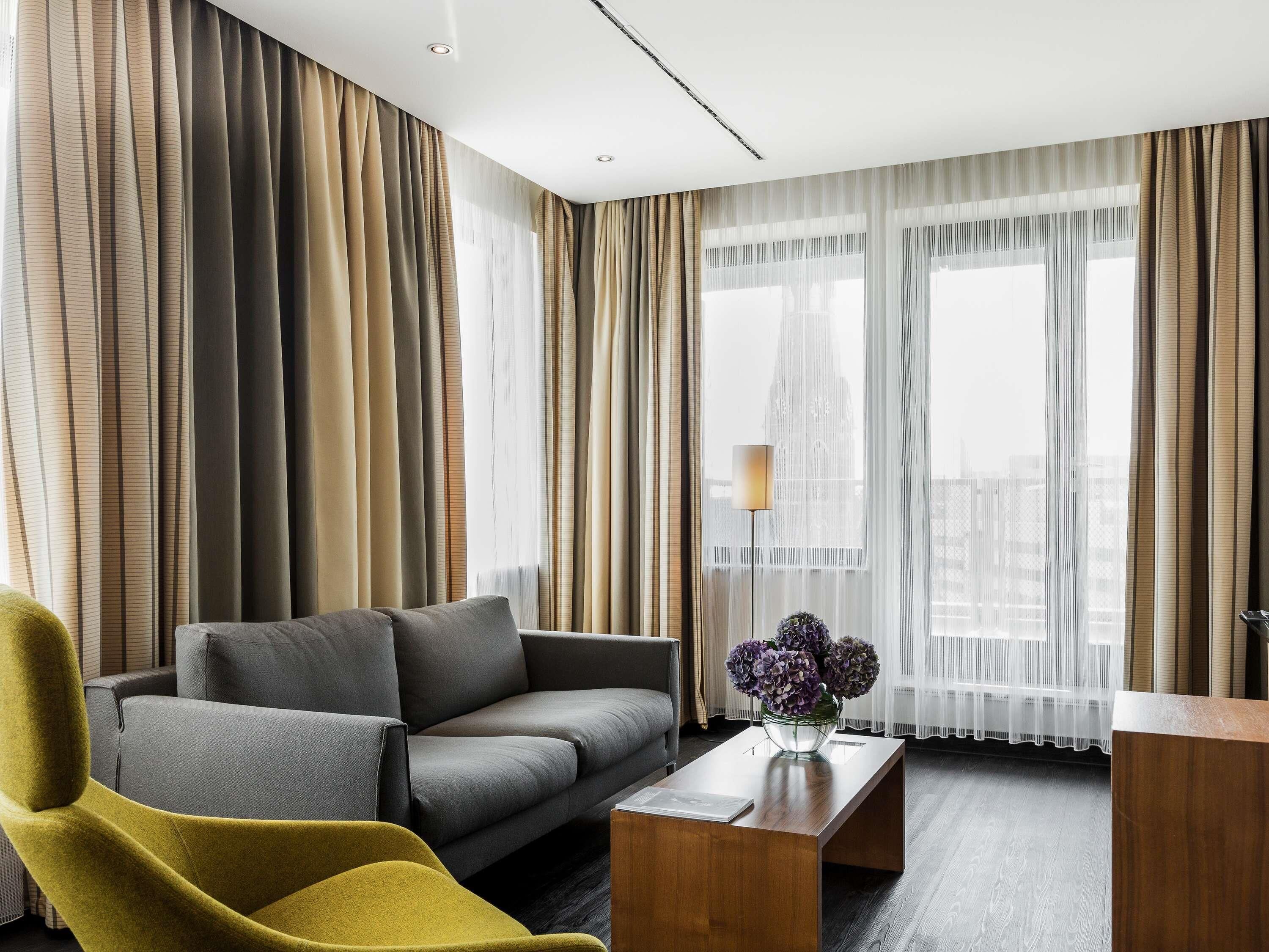 A modern hotel room with a sofa, armchair, and a coffee table with a vase of flowers.