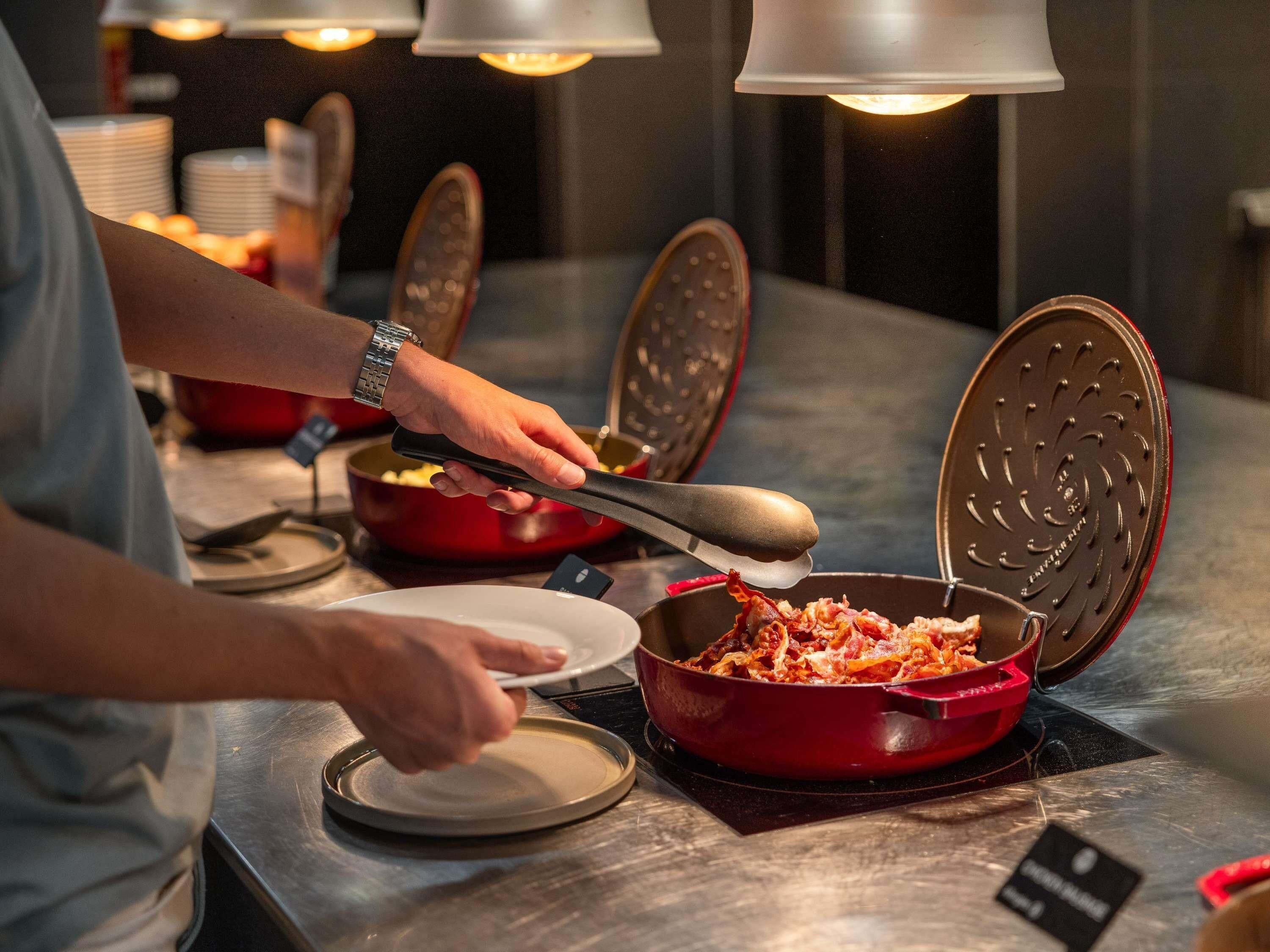 A person using a waffle iron on a red pan, with a plate and a spoon nearby.