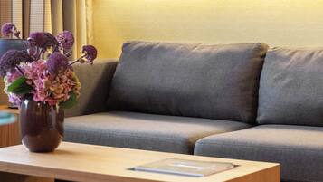 Een moderne woonkamer met een grijze bank, een houten salontafel en een vaas met paarse bloemen.
