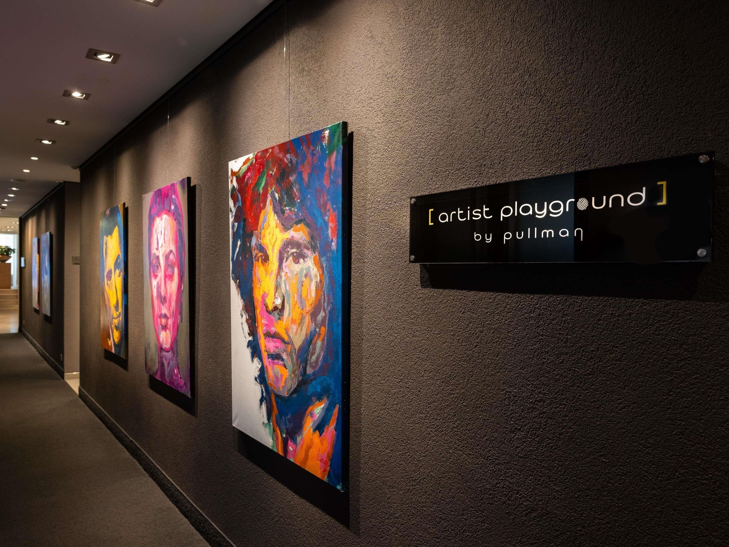 En gang med en række farverige malerier på væggen og et skilt, der siger 'artist playground by pullman'.