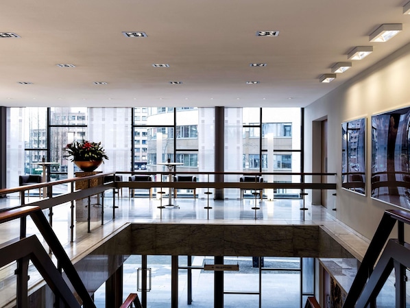A modern hotel lobby with a reception desk, seating area, large windows, and a view of the cityscape.