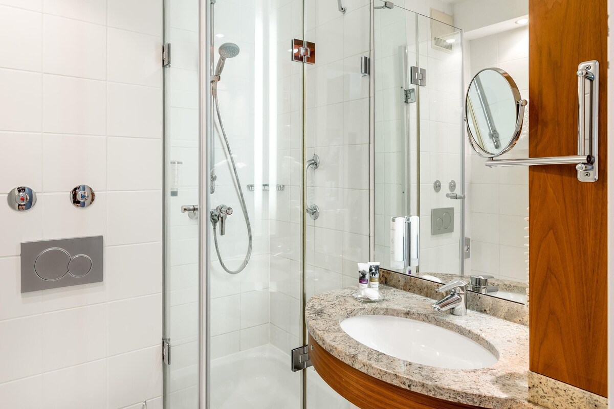 A modern bathroom with a glass-enclosed shower, a granite countertop sink, and a wooden vanity.