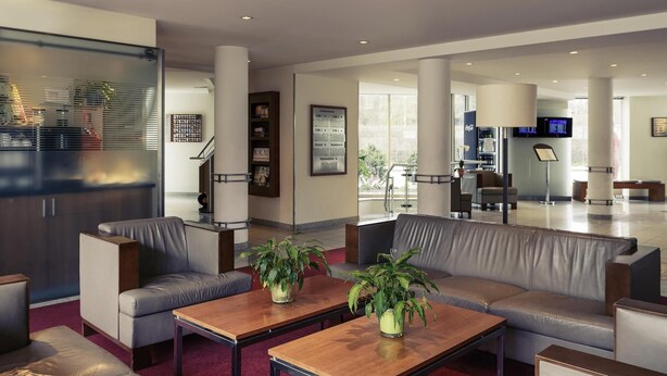 Eine moderne Lobby mit Ledersofas, Holztischen und Pflanzen in Töpfen.