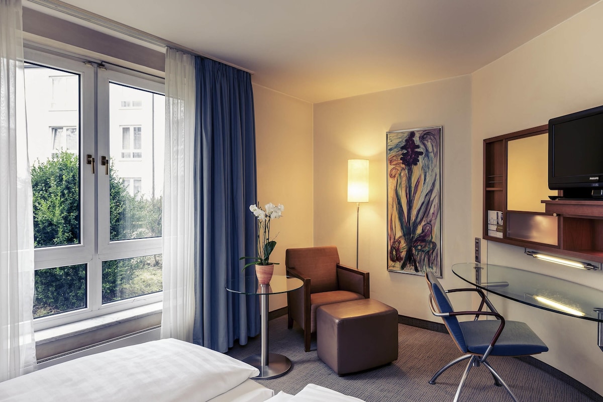 A hotel room with two beds, a desk, a chair, a TV, and a window with curtains.