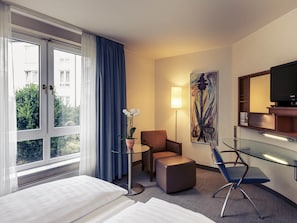 Habitación de hotel con dos camas, un escritorio, una silla, un televisor y una ventana con cortinas.