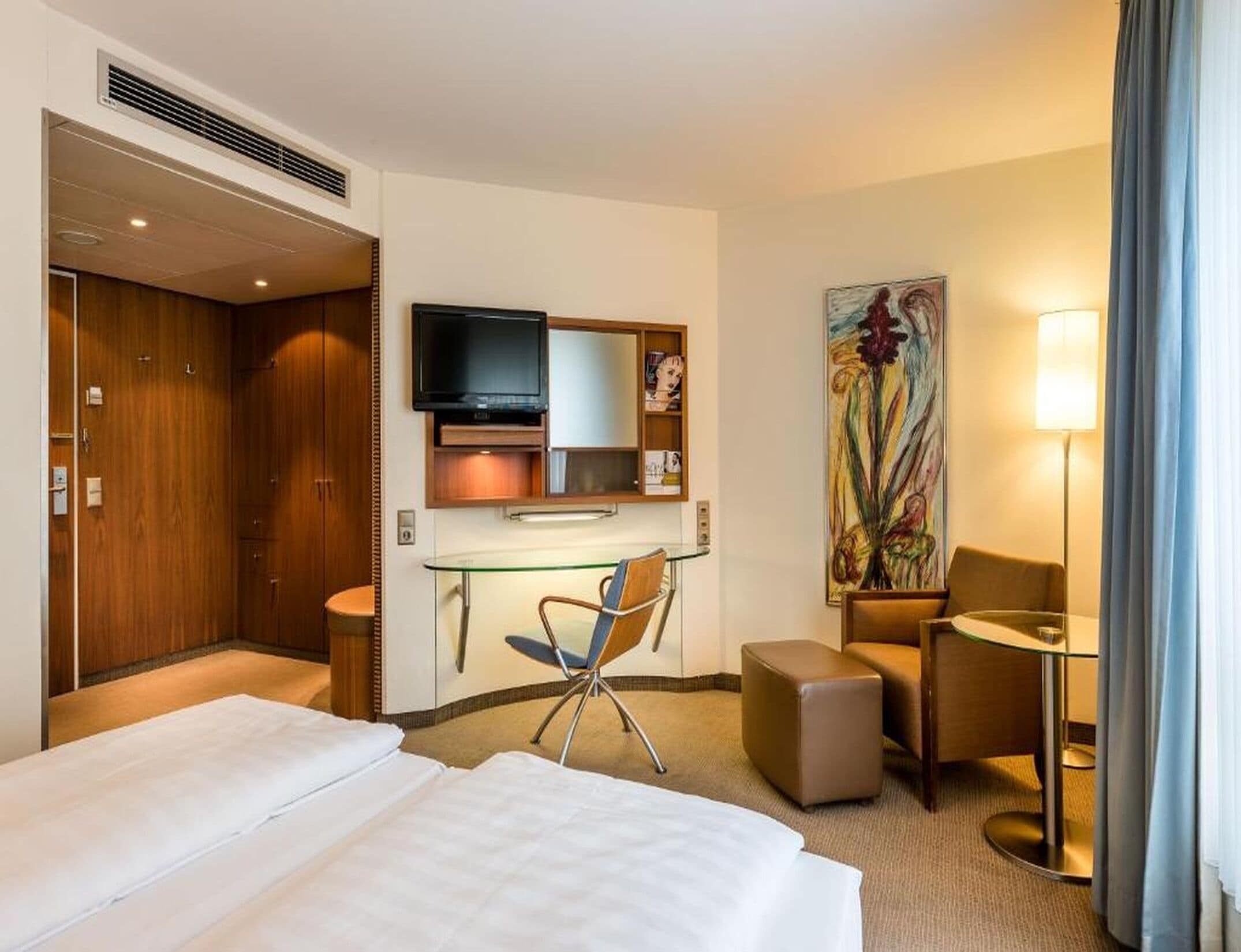Une chambre d’hôtel équipée d’un lit, d’un bureau, d’une chaise, d’une télévision, d’œuvres d’art et d’une lampe.