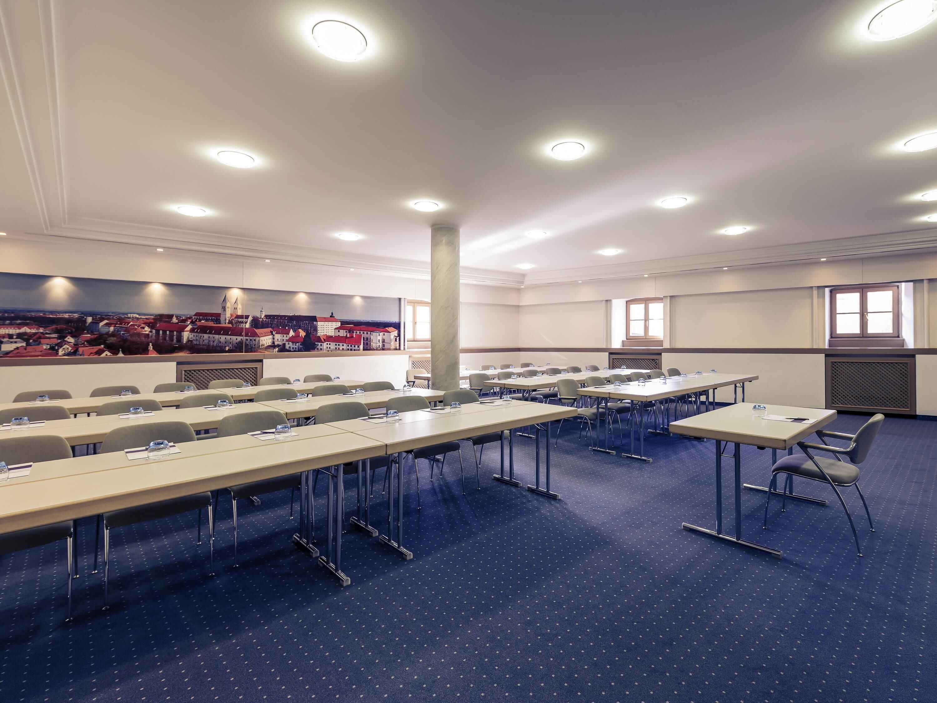 Une salle de conférence dotée de plusieurs tables, de chaises et d’une fresque représentant un paysage urbain sur l’un des murs.