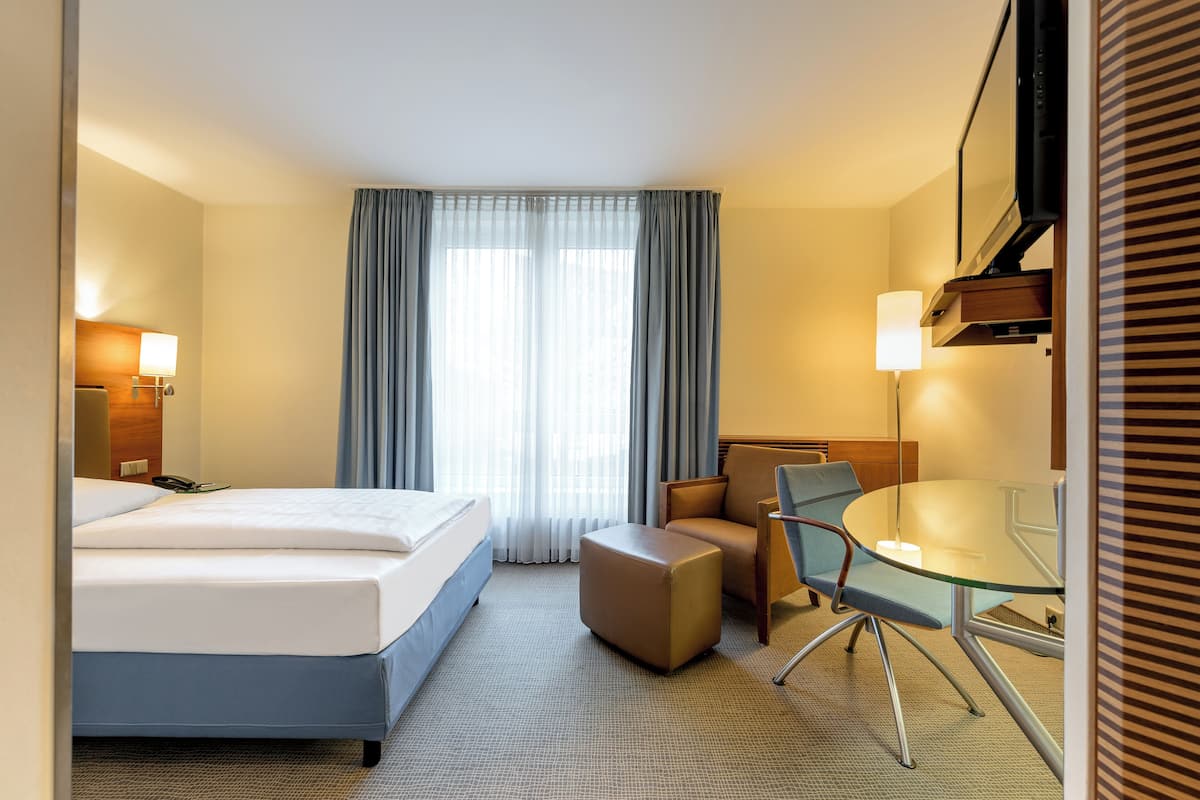 A hotel room with a bed, a desk, a chair, and a television.