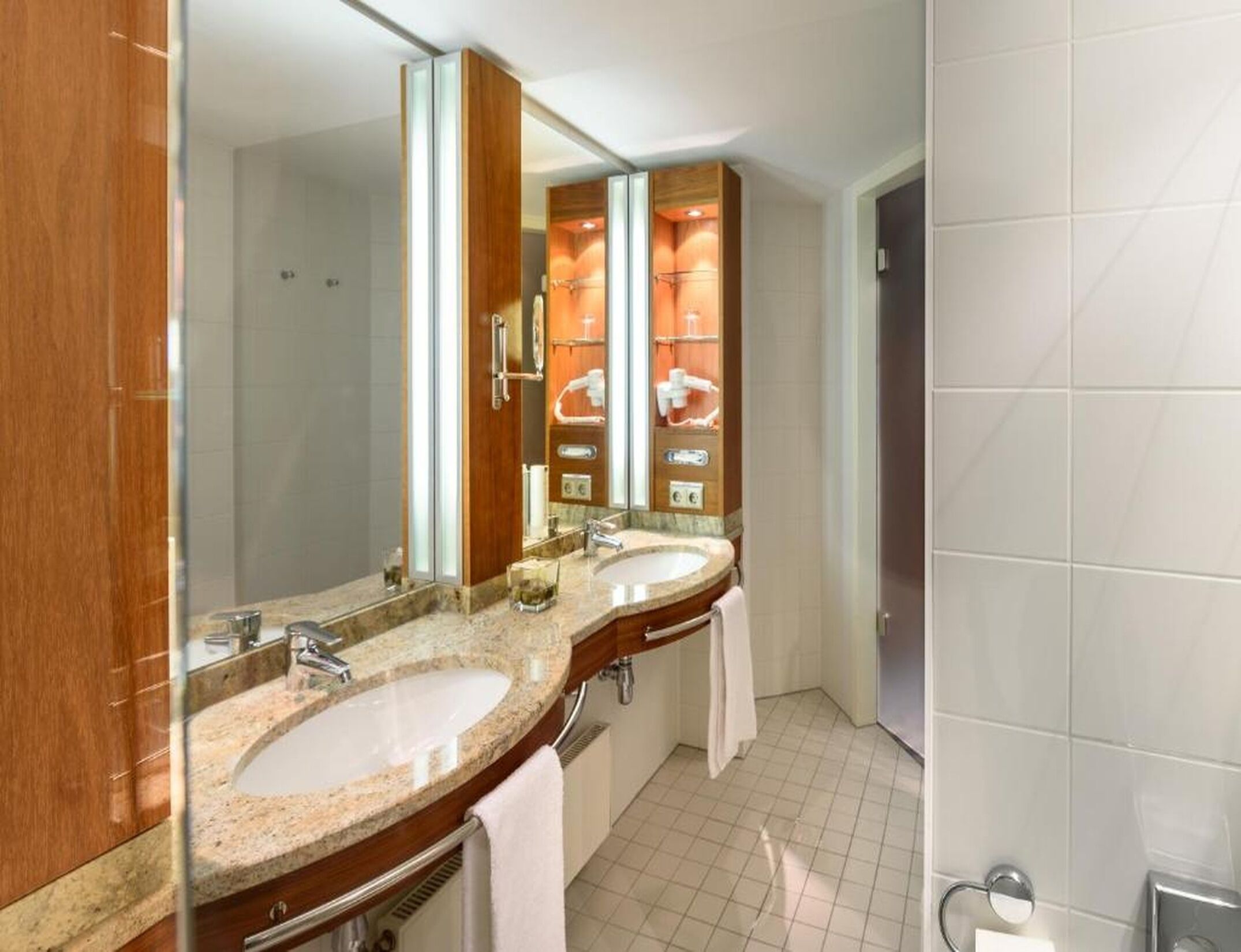 A hotel bathroom with two sinks, a large mirror, and a shower area.
